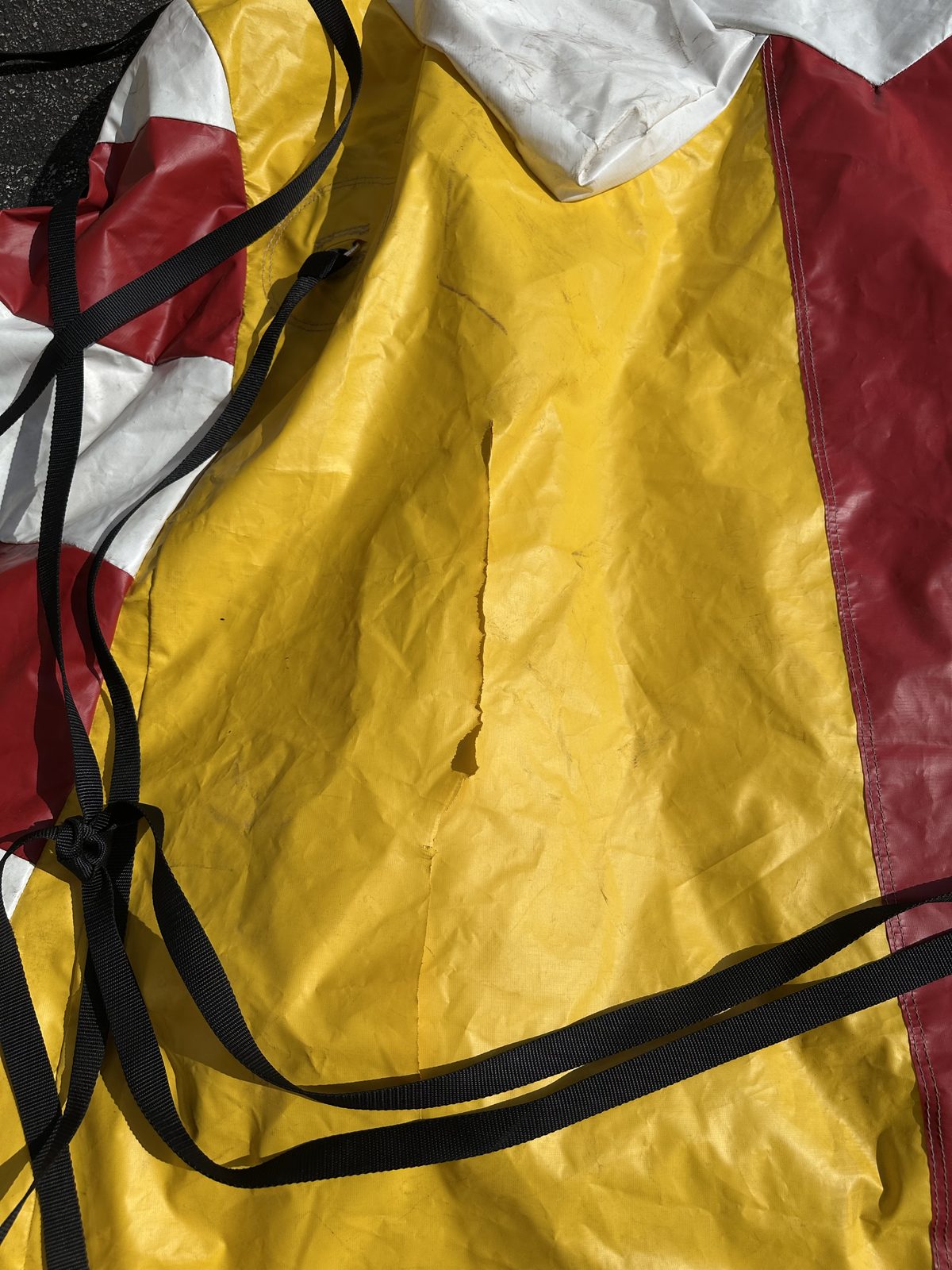 A torn yellow vinyl inflatable with tether straps, brought in for repair